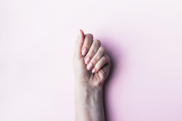 Woman's hand with a beautiful manicure - pink nude nails with small black dots on a pink background