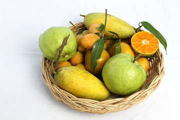 Fruits such as oranges, mangoes, guava are packed in wicker baskets and set on a white cloth as a background.