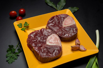 
ossobuco slices on yellow plate with parsley, leek and bay leaf on black background