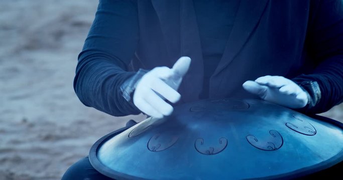 a man in a venetian mask on the seashore plays the glucophone against the background of a burning old piano
