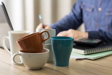 used coffee cups on the office desk and a man working hard drink several cups of coffee to stay refresh in the background.
