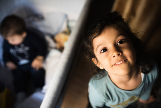 Little girl looks at camera as her little brother plays in the crib