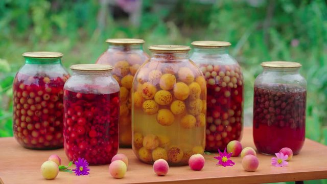 Jars with compote on table. Sealed glass jars with kompot placed on table near flowers and fruits on summer day in garden
