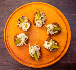 slices of black bread with meat pate decorated with pickles and onions on a round wooden tray....