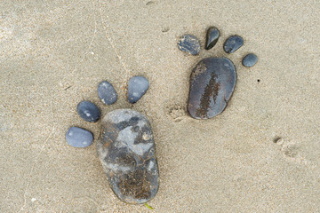 Two pebble footprints on the surface of the desert sea sand. Games on the sand and on the beach. A copy of the space