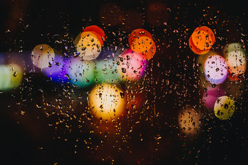 Colorful blurred defocused traffic lights on the black background through the window with raindrops.