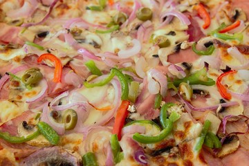 Freshly baked pizza with mozzarella cheese, salami, mushrooms, tomato sauce, olives, green peppers, and onions ingredients. Closeup, shallow depth of field