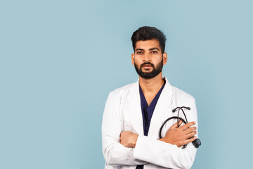 Handsome modern Indian / Asian doctor with stethoscope, in uniform on blue background