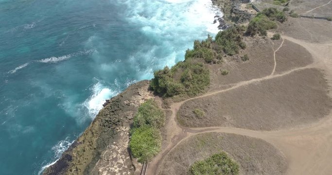 Drone shot flying backwards and tilting up to reveal waves breaking on wild rocky coastline