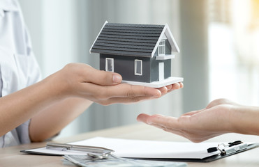 Hand a real estate agent, hold the home model, and explain the business contract, rent, buy, mortgage, loan, or home insurance to the buyer woman