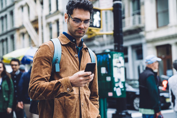 Thoughtful Hispanic man with smartphone on busy New York street