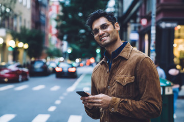 Cheerful ethnic young man with smartphone on street