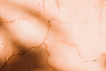 Fototapeta premium An old wall with orange cracks. Plaster is falling off.Shadows fall on the wall.