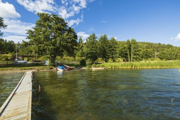 Beautiful summer natural landscape view. View from wooden bridge on lake coast line with boats and green forest trees.