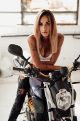 Plakat A blond girl rides modern custom motorcycle in the bright garage