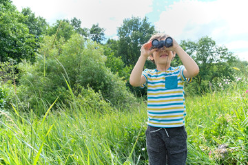 Young boy in a field looking through binoculars.