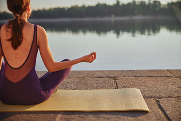 Rear shot of young woman practicing yoga in the morning near river