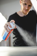 Selective focus of craftsman holding spray tack glue while working with screen printing machine 