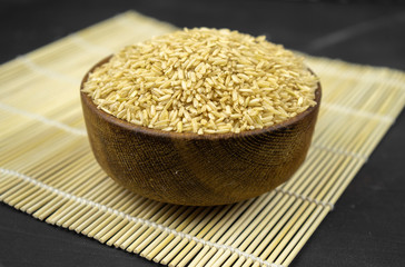 brown rice in a wooden bowl on bamboo mat, asian kitchen background on black