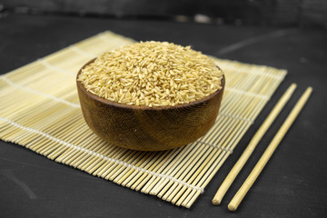 brown rice in a wooden bowl on bamboo mat, asian kitchen background on black
