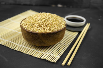 brown rice in a wooden bowl on bamboo mat, asian kitchen background on black