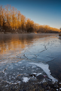 Bank of the river Isar near Garching in Bavaria on sunny cold winter day with ice, trees and snow