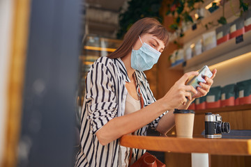 Female in mask is reading the message in cafe