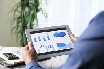 man's hand working on digital tablet at office desk, using self created chart 