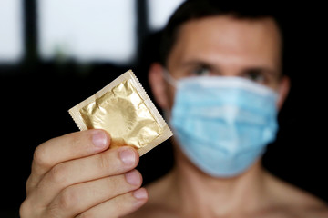 Condom in male hands close up, safe sex during coronavirus pandemic. Man in medical face mask giving condom in package, contraception concept