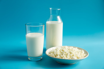 Milk in a glass Cup and bottle and cottage cheese in bowl. Dairy products on a bright, blue background close up.