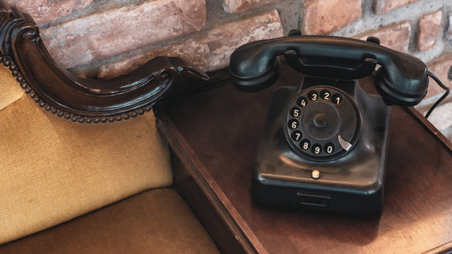 Elegant vintage old phone on elegant wooden and textile upholstery vintage sofa against brick wall antique decoration