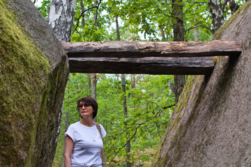 woman in frame of huge boulders covered with green moss in wild forest