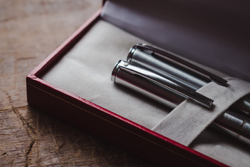 Close-up of silver fancy office pens in a red box on wooden table