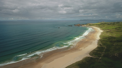 Aerial view sandy beach: ocean foamy waves drops to coastline in White Beach, Antrim County. Seascape of picturesque nature of Northern Ireland. Dramatic summer scenery in day