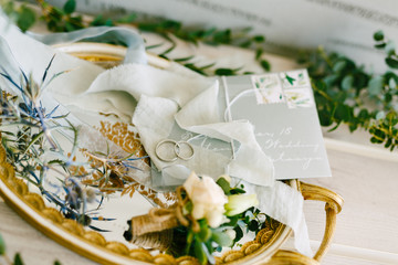 Two wedding rings for the bride and groom and on a tray with golden patterns, boutonniere, ribbon and letter.