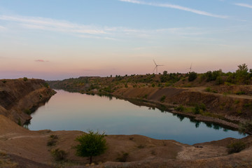 Wind turbine rises above small lake at the sunset. Renewable electricity generation theme.