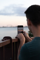Man taking a photo on a smartphone of a landscape at sunset