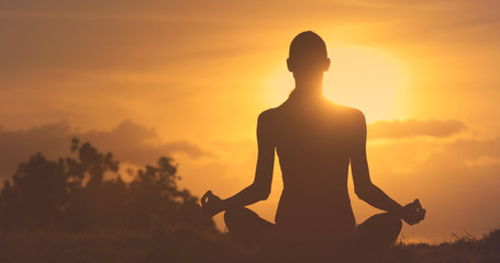 silhouette of a female meditating during golden sunrise. 