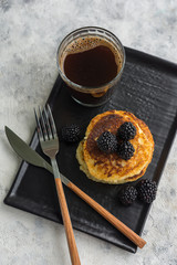 Cottage cheese pancakes with blackberries on a dark plate with cutlery and light background