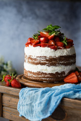 Naked cake with cream, decorated with strawberry and mint. Chocolate cake.