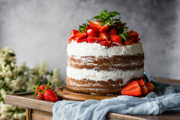 Naked cake with cream, decorated with strawberry and mint. Chocolate cake.