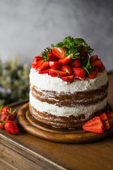 Naked cake with cream, decorated with strawberry and mint. Chocolate cake.