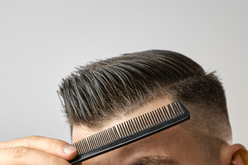 Close up young man combing his hair with a plastic comb. Styling hair after barbershop. 