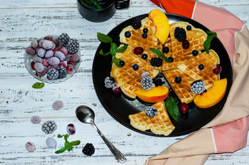 Crispy Viennese waffles on a black matte plate with blackberries, kizil and grapes poured with May honey. Breakfast. Vitamins. Homemade pastries. Appetizing background with the ability to insert text.
