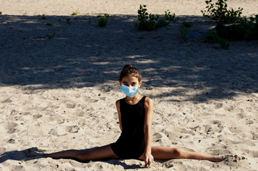 A gymnast girl in a protective medical mask, dressed in a sports swimsuit, performs gymnastic...