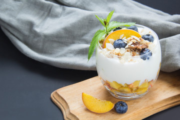 Healthy blueberry, peach and walnut parfait in a glass on a dark background