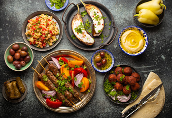 Middle eastern or Mediterranean dinner with grilled kebab, falafel, roasted and fresh vegetables, assorted Arabic meze and appetizers served on rustic background table. Dinner table overhead 
