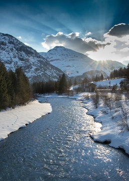 Winterliche Flusslandschaft mit Schnee und Bergen bei Sonnenuntergang