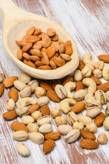 Close-up of dried almonds in a wooden spoon on a wooden background. Various varieties of nuts on a wooden table.