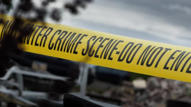 Police Crime Scene Cordon Tape Around Junkyard Car.  There is an overcast sky and light rainfall. Suggestive of the scene of a murder or hiding of a body.